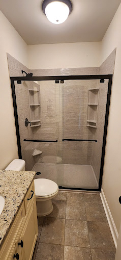 Contemporary bathroom design showcasing a sleek wall-mounted sink with a minimalist mirror above it, against a backdrop of dark gray and wood-effect tiles. The space features a modern toilet with eco-friendly flushing options, accented by a vertical green living wall, adding a touch of nature and sustainability to the refined and functional aesthetic.